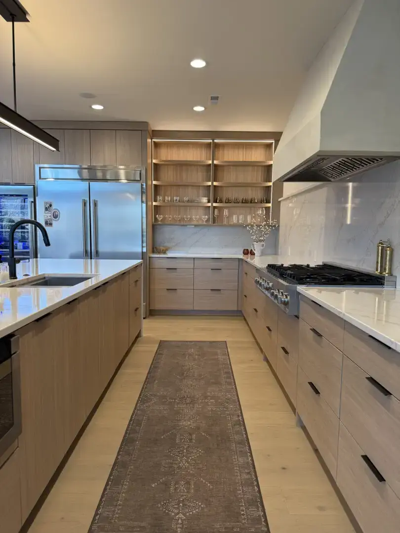 Modern kitchen with light wood cabinets, stainless steel appliances, and a runner rug.