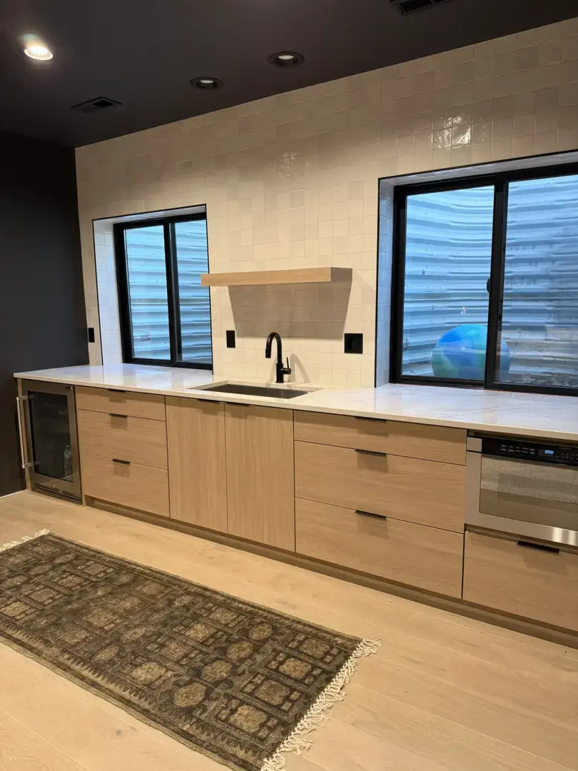 Modern kitchen with light wood cabinets, white tile backsplash, and black fixtures.